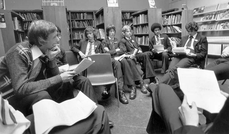 Students participate in a group discussion and debate in a school library, illustrating themes of critical thinking, civil discourse, and understanding different perspectives explored in Elliot Ackerman's essay A Man Should Know: How to Form an Opinion.