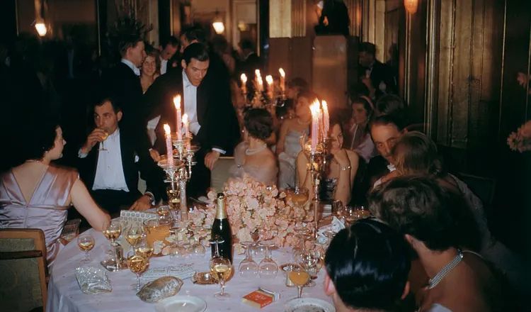 Guests gather around a candlelit dinner table during an elegant evening gathering, illustrating themes of hospitality, friendship, hosting, and creating meaningful experiences explored in Elliot Ackerman's essay A Man Should Know: How to Host.