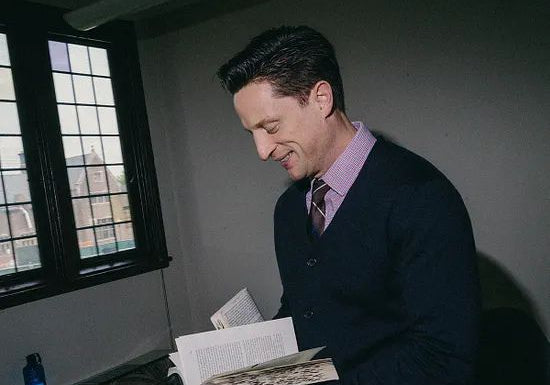 Elliot Ackerman reads from an open book in a study, illustrating themes of reading, literature, lifelong learning, and the transformative power of books explored in A Man Should Know: How to Read.