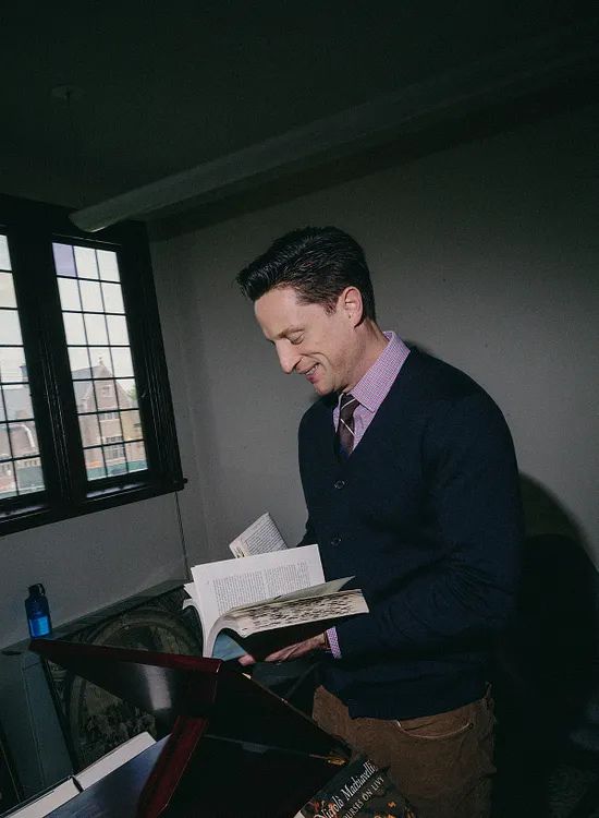 Elliot Ackerman reads from an open book in a study, illustrating themes of reading, literature, lifelong learning, and the transformative power of books explored in A Man Should Know: How to Read.