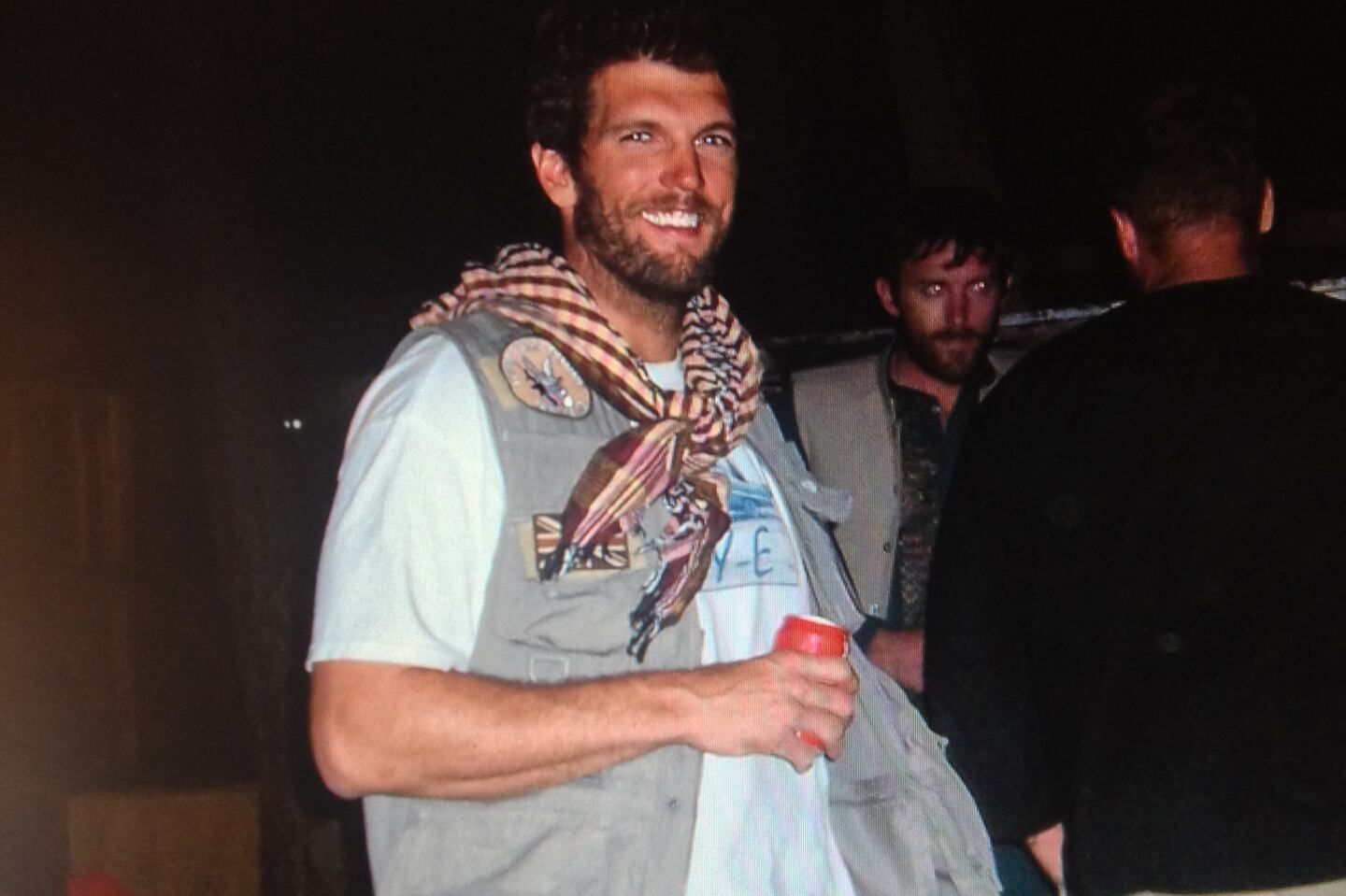 MSgt Aaron Torian stands smiling at night wearing a tactical field vest and a patterned scarf while holding a red beverage can.