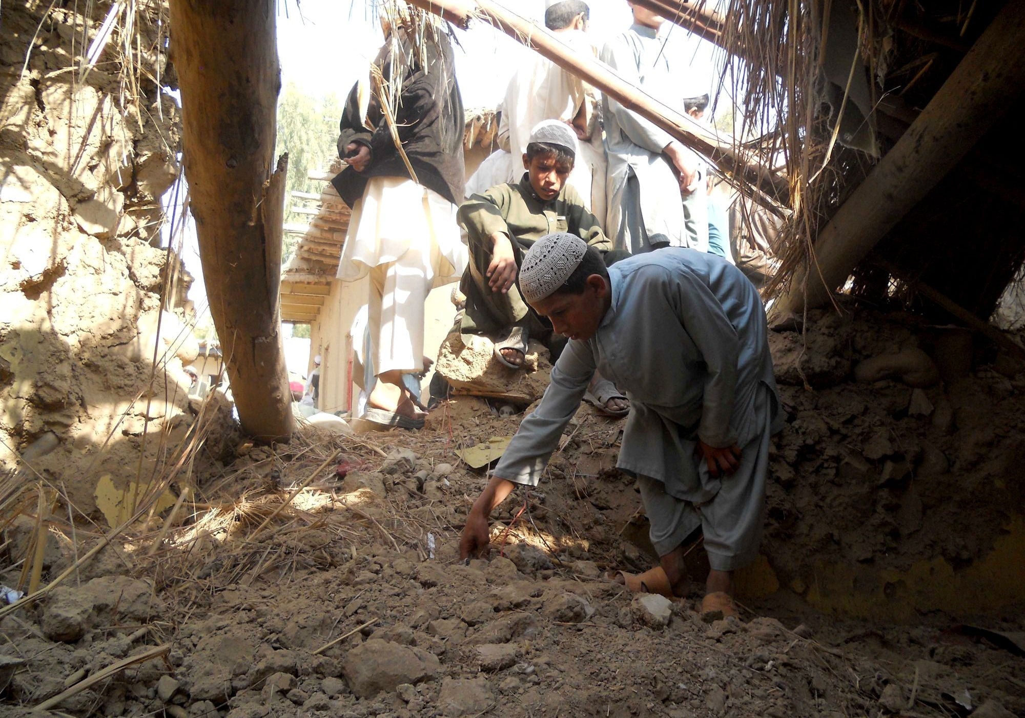 Local residents examine the wreckage of a mud-brick structure in a drone strike's aftermath.