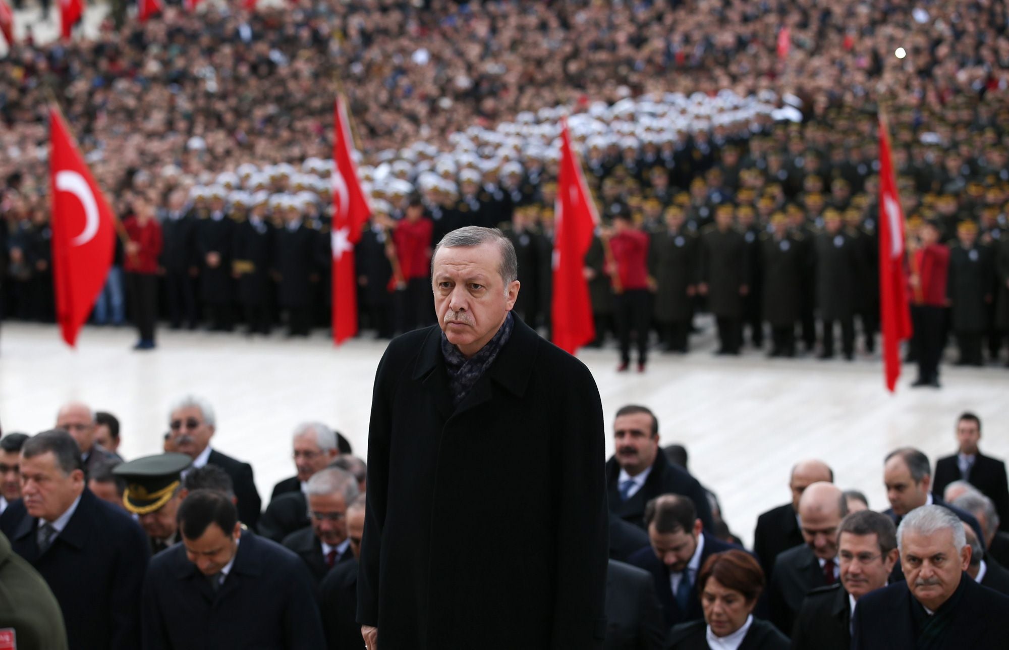 Turkish President Recep Tayyip Erdoğan stands before a crowd with Turkish flags at a state ceremony.