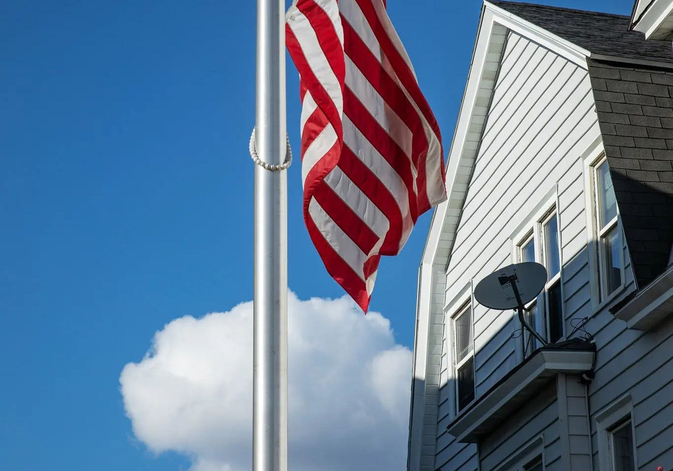 American flag flying at half-staff on a residential flagpole beneath a clear blue sky, symbolizing national mourning, remembrance, sacrifice, and collective grief during the COVID-19 pandemic.