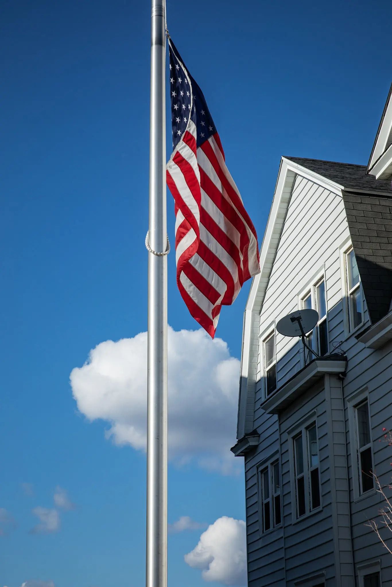 American flag flying at half-staff on a residential flagpole beneath a clear blue sky, symbolizing national mourning, remembrance, sacrifice, and collective grief during the COVID-19 pandemic.