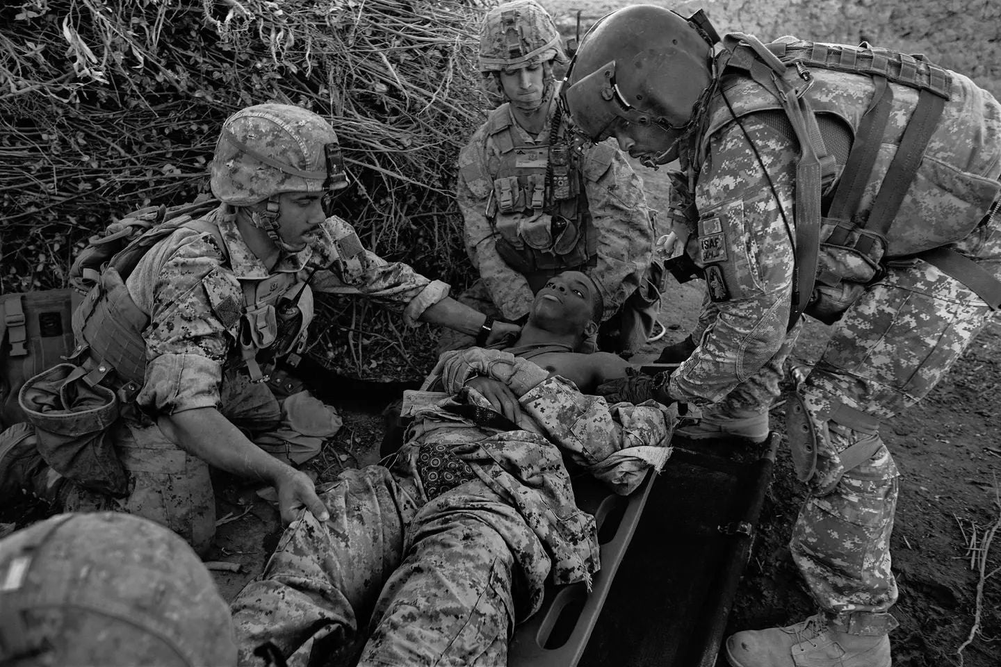 U.S. Marines and an Army flight medic provide emergency medical care to a wounded Afghan civilian on a stretcher during combat operations in Afghanistan, highlighting the human cost of America's longest war.