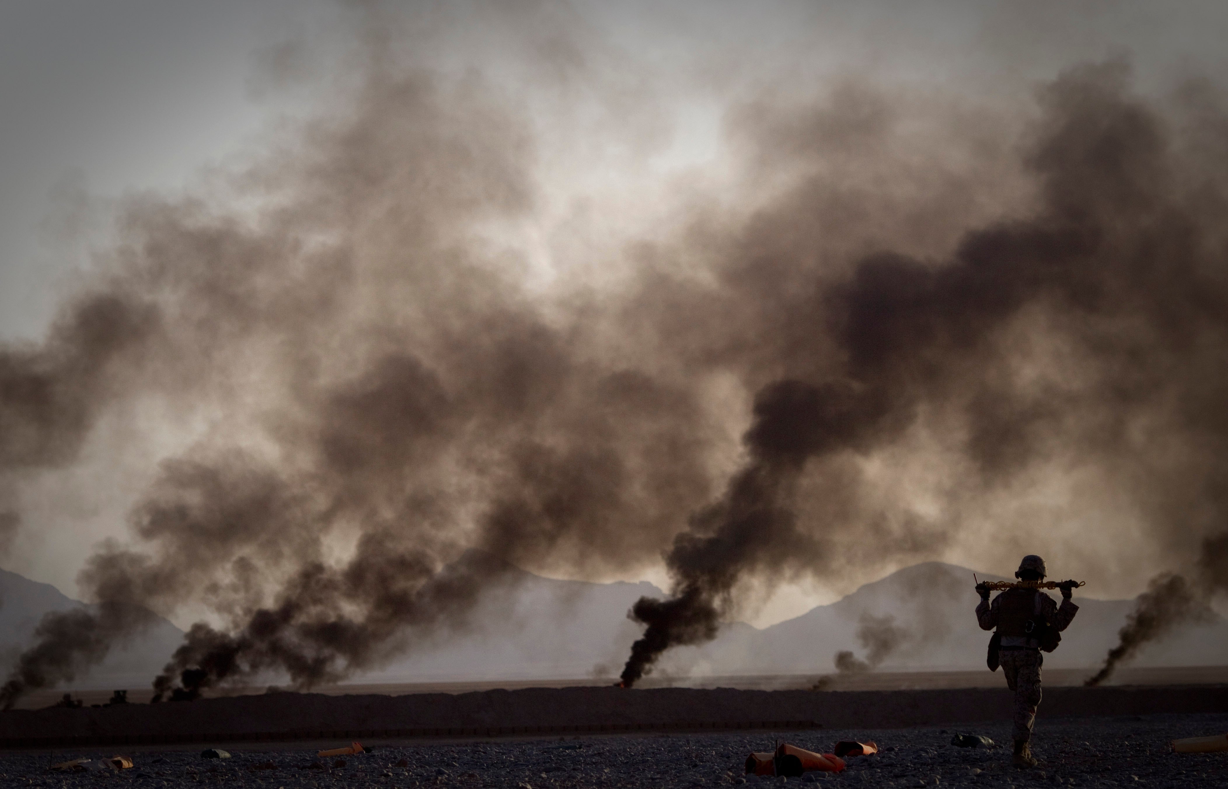 A soldier walks alone through a smoke-filled desert landscape.