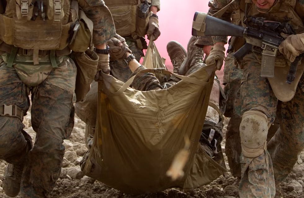 Marine Corps service members carry a wounded Marine in a soft stretcher during a combat casualty evacuation exercise, highlighting battlefield teamwork, combat medicine, and the realities of modern military operations.