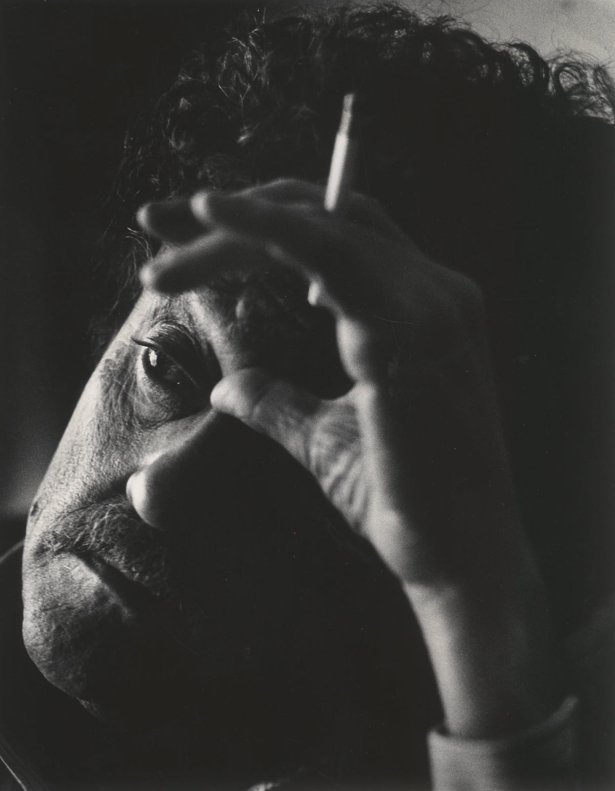 A dramatic black-and-white close-up portrait of a man's face partially obscured by his hand, holding a cigarette.
