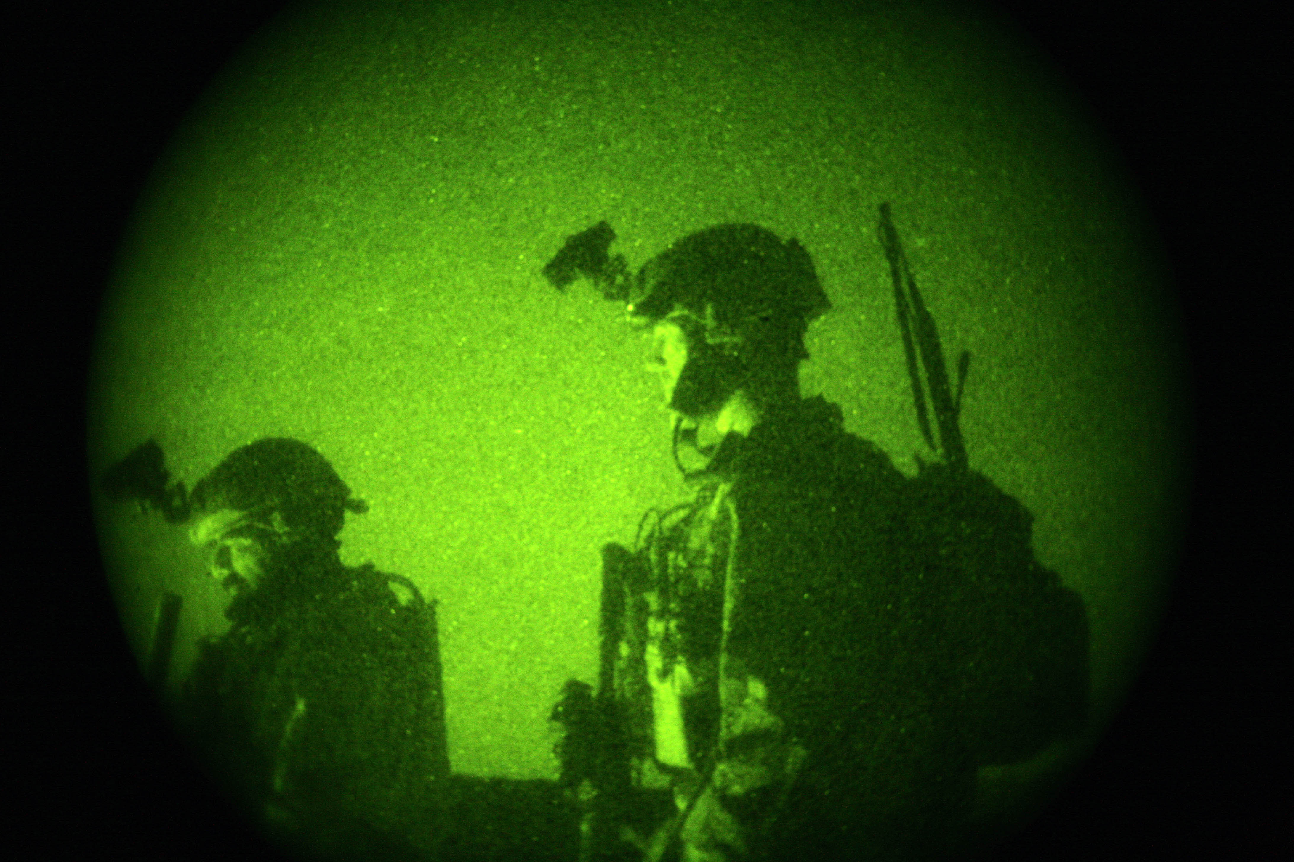 Two special operations soldiers seen through green night-vision optics, wearing helmets and combat gear.