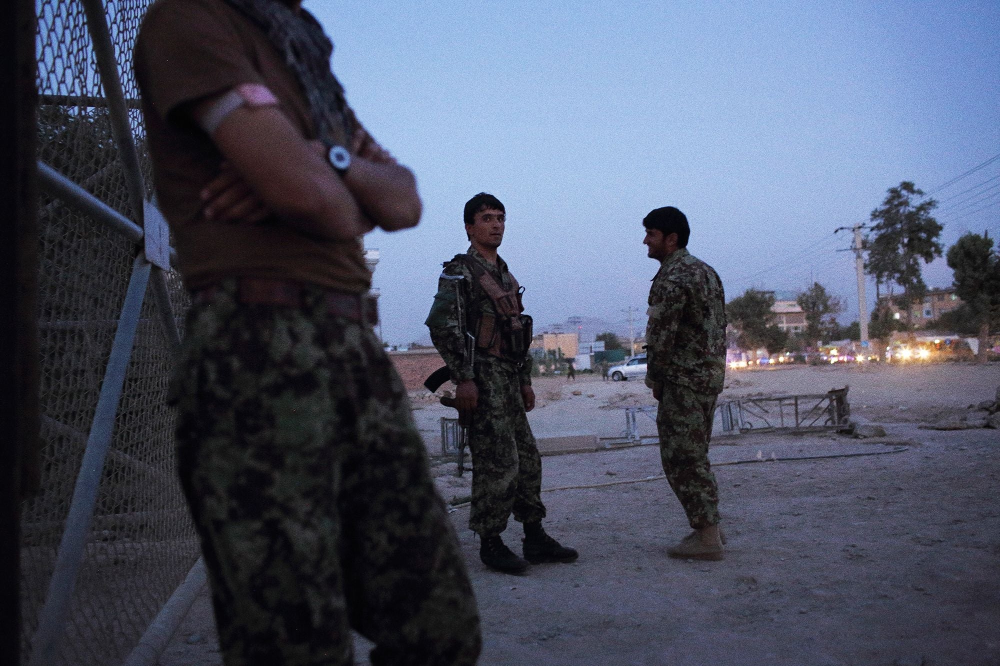 Afghan National Army soldiers stand near a checkpoint fence at dusk.