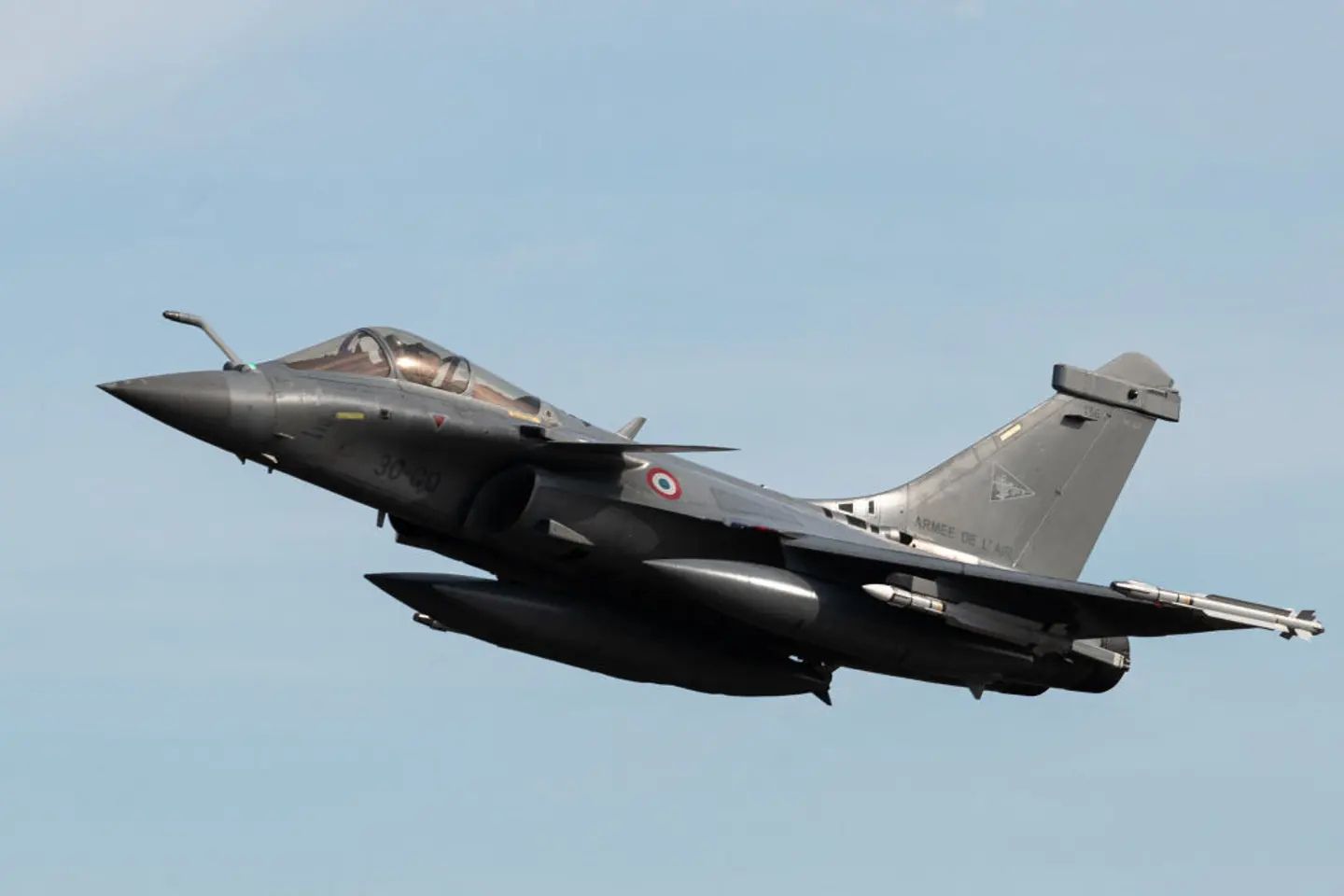A French Air and Space Force Dassault Rafale multirole fighter jet flies in clear skies carrying external fuel tanks and air-to-air missiles, illustrating modern NATO air power and advanced Western combat aviation.