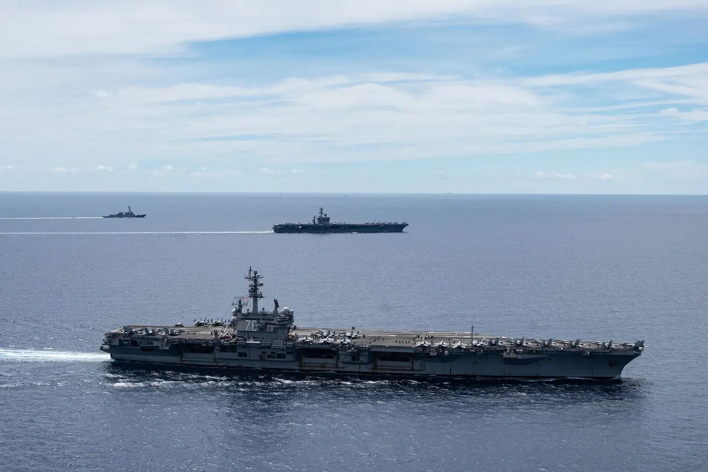 Three U.S. Navy warships, including two aircraft carriers and an escort vessel, sail in formation across the open Pacific Ocean during a naval deployment, illustrating American maritime power and strategic operations in the Indo-Pacific region.