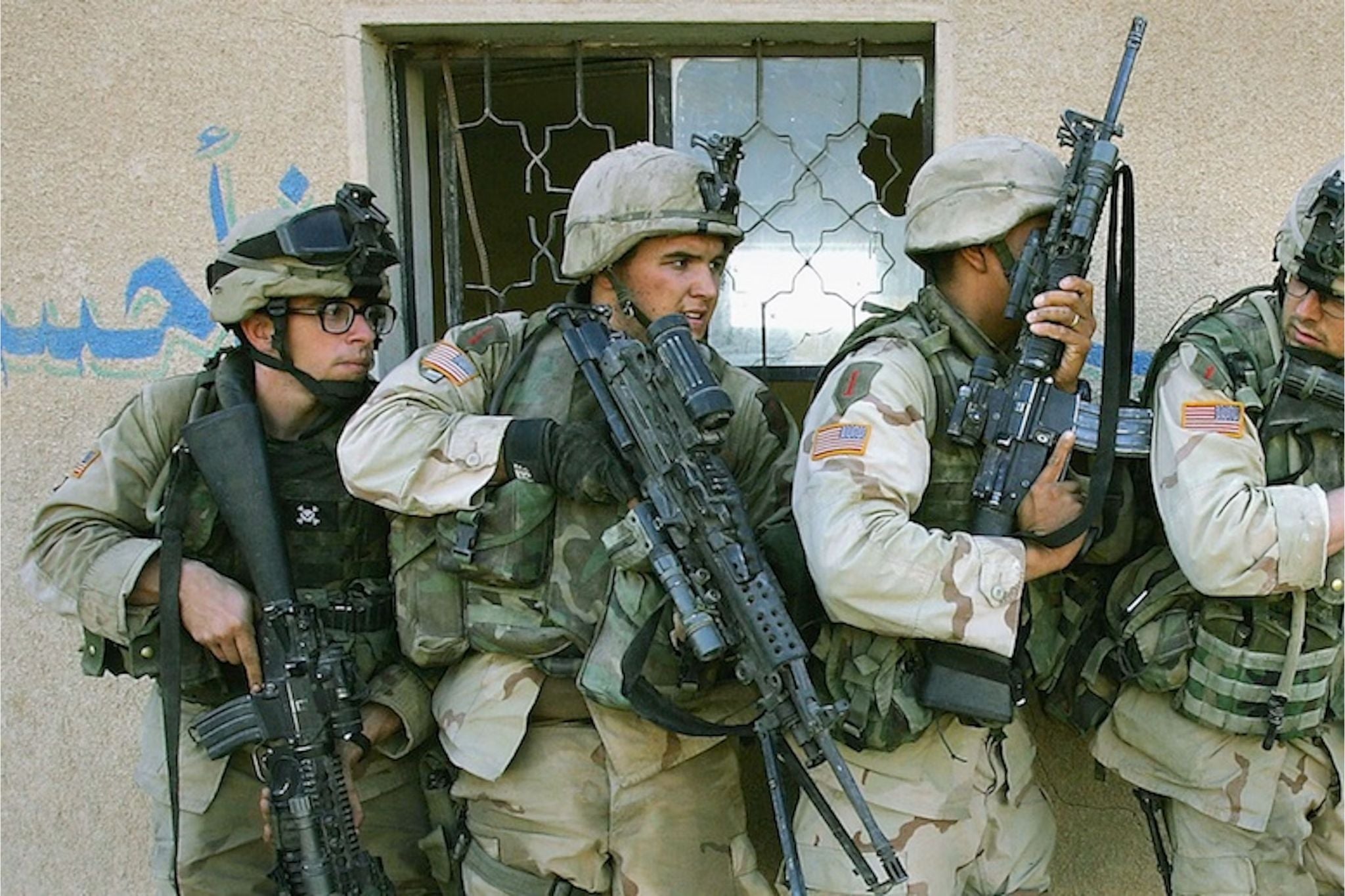 U.S. Marines stack outside a damaged building during urban combat in Fallujah, Iraq, preparing to move through the doorway while scanning for threats.