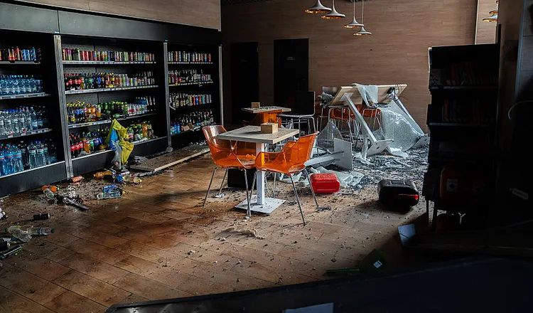 Damaged gas station interior in Yahodyn, Ukraine, after a Russian drone strike, showing shattered windows, debris, overturned furniture, and damaged displays.