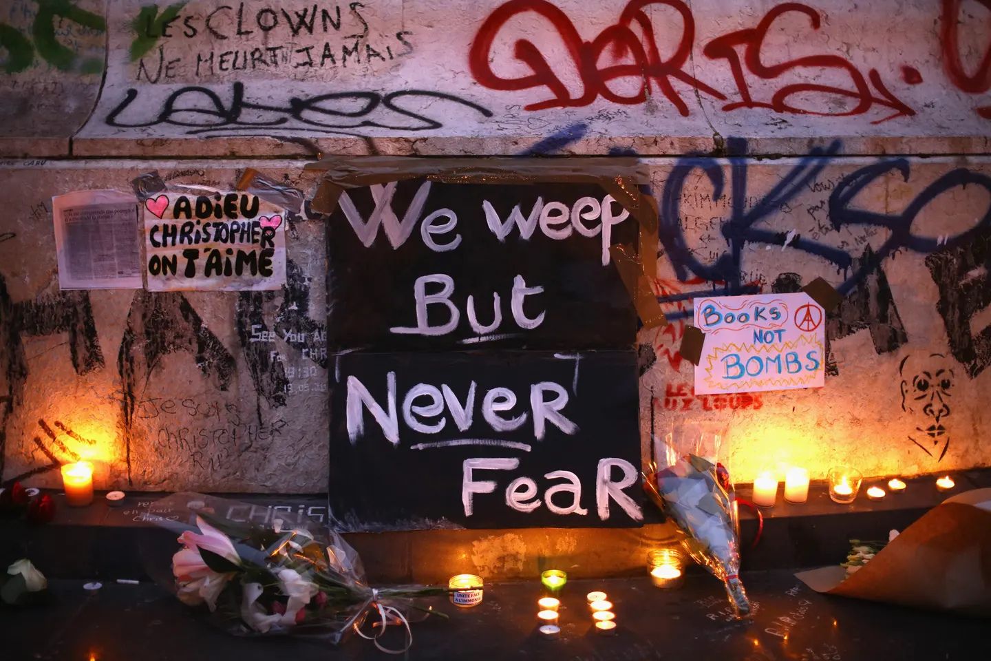Memorial honoring victims of the November 2015 Paris terrorist attacks, with candles, flowers, handwritten signs, and graffiti-covered walls.