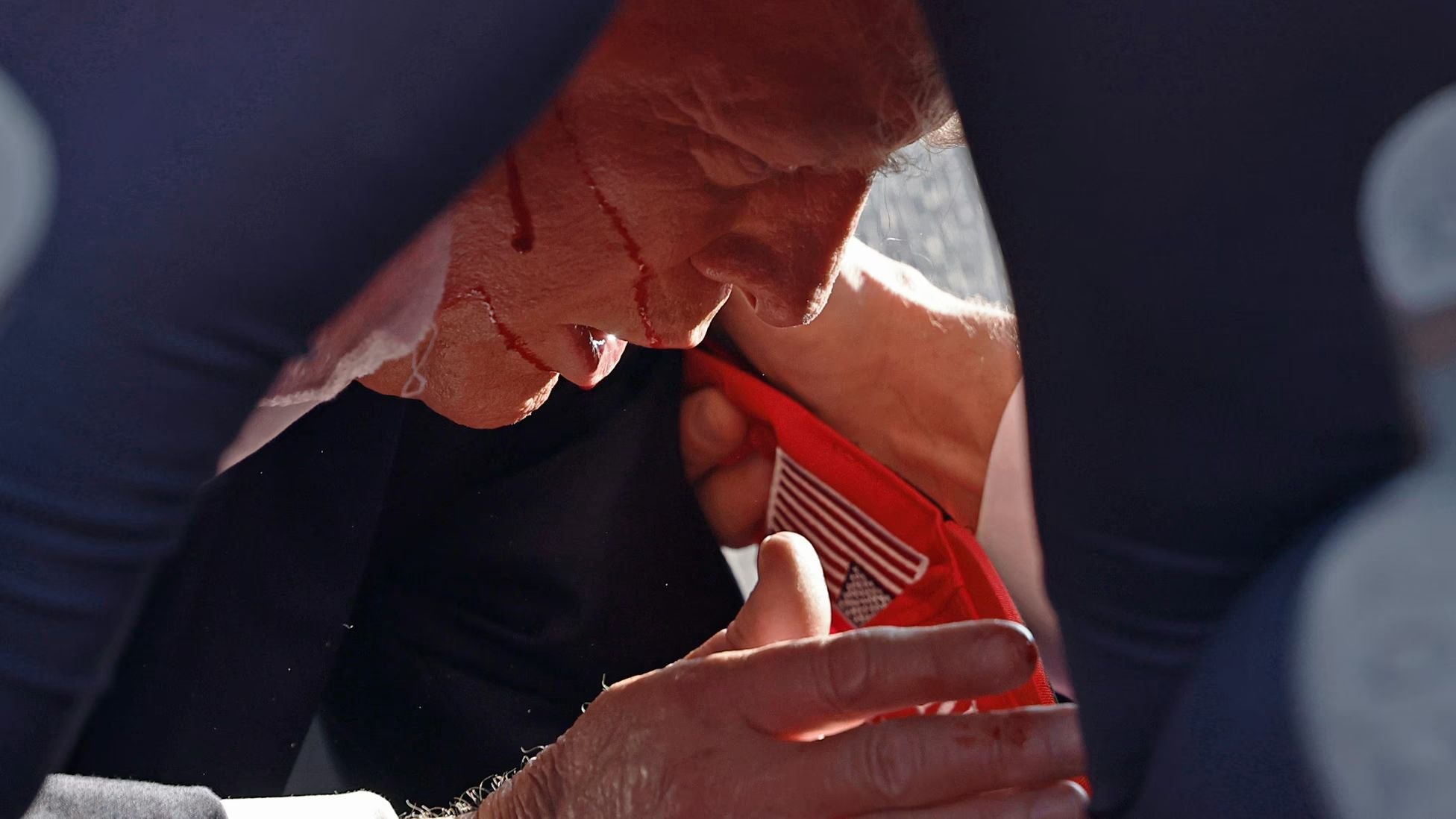 Former President Donald Trump, blood visible on his face after the attempted assassination at a campaign rally in Butler, Pennsylvania, is surrounded by U.S. Secret Service agents as he is escorted from the stage.