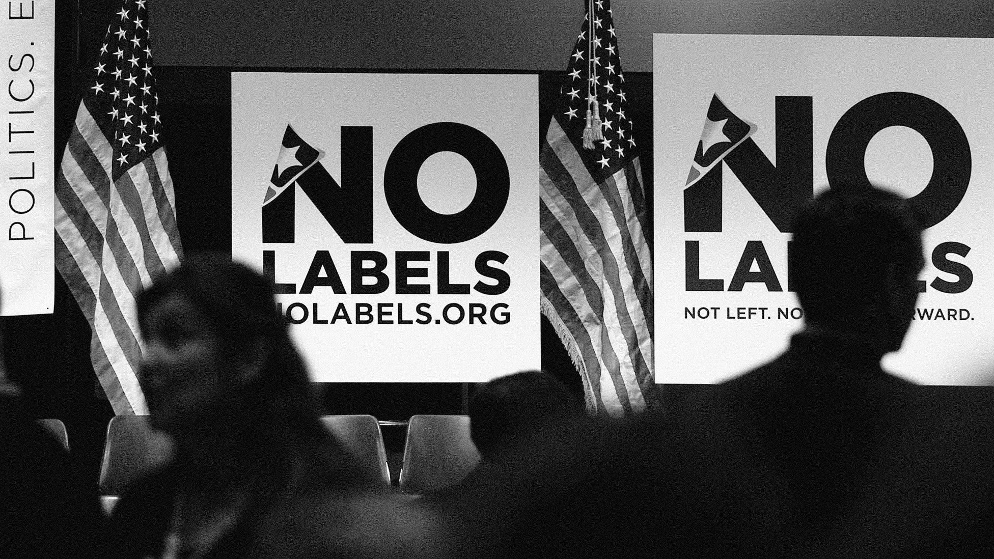 Attendees move through a No Labels political event as American flags flank large No Labels signs in the background.