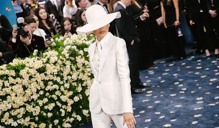 Zendaya attends the 2025 Met Gala wearing a tailored white three-piece Louis Vuitton pantsuit and oversized wide-brimmed white hat, interpreting the "Superfine: Tailoring Black Style" theme with a minimalist menswear-inspired look.