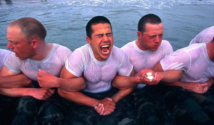 U.S. Navy Sailors participate in a cold-water endurance training exercise, linked arm-in-arm in the surf while enduring physical and mental stress during a warrior training event.