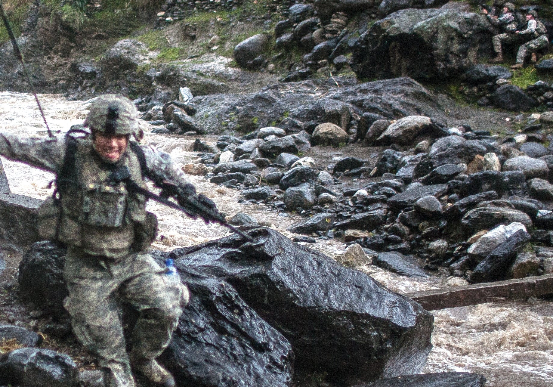 Book cover of 'The Fighters: Americans in Combat in Afghanistan and Iraq' by C.J. Chivers, showing a soldier crossing a rocky river in a mountainous valley.