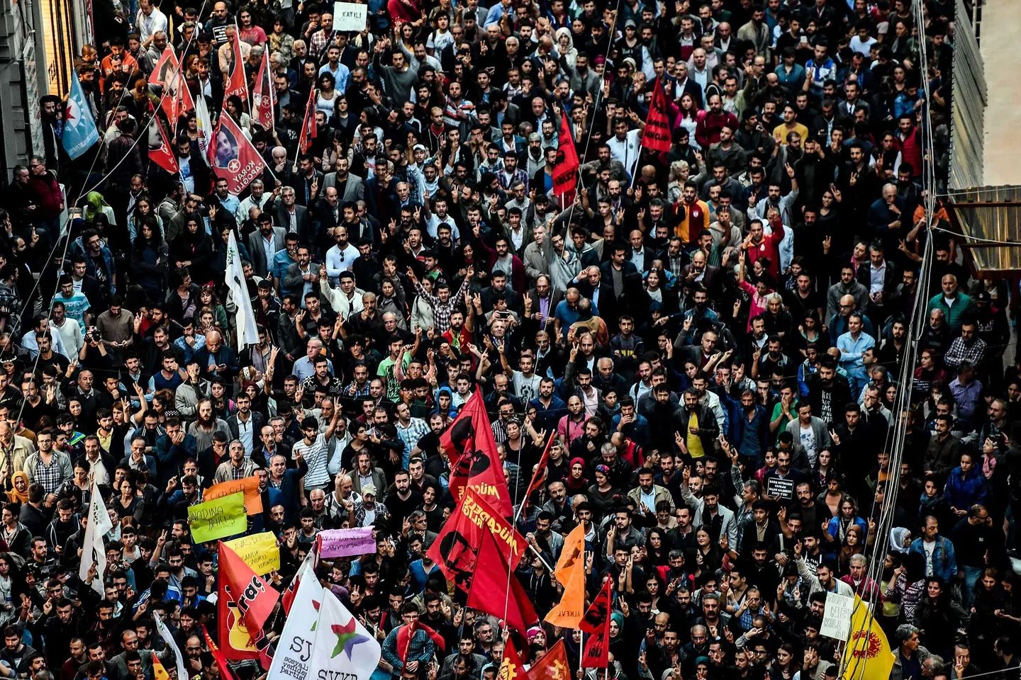 Large crowd of demonstrators marching through the streets of Ankara during a public protest, with participants carrying flags and banners and many raising peace signs.