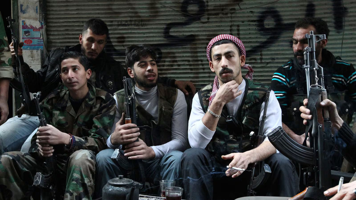 Armed Syrian opposition fighters gather inside a storefront in northern Syria, seated together with AK-pattern rifles while drinking tea and smoking cigarettes.