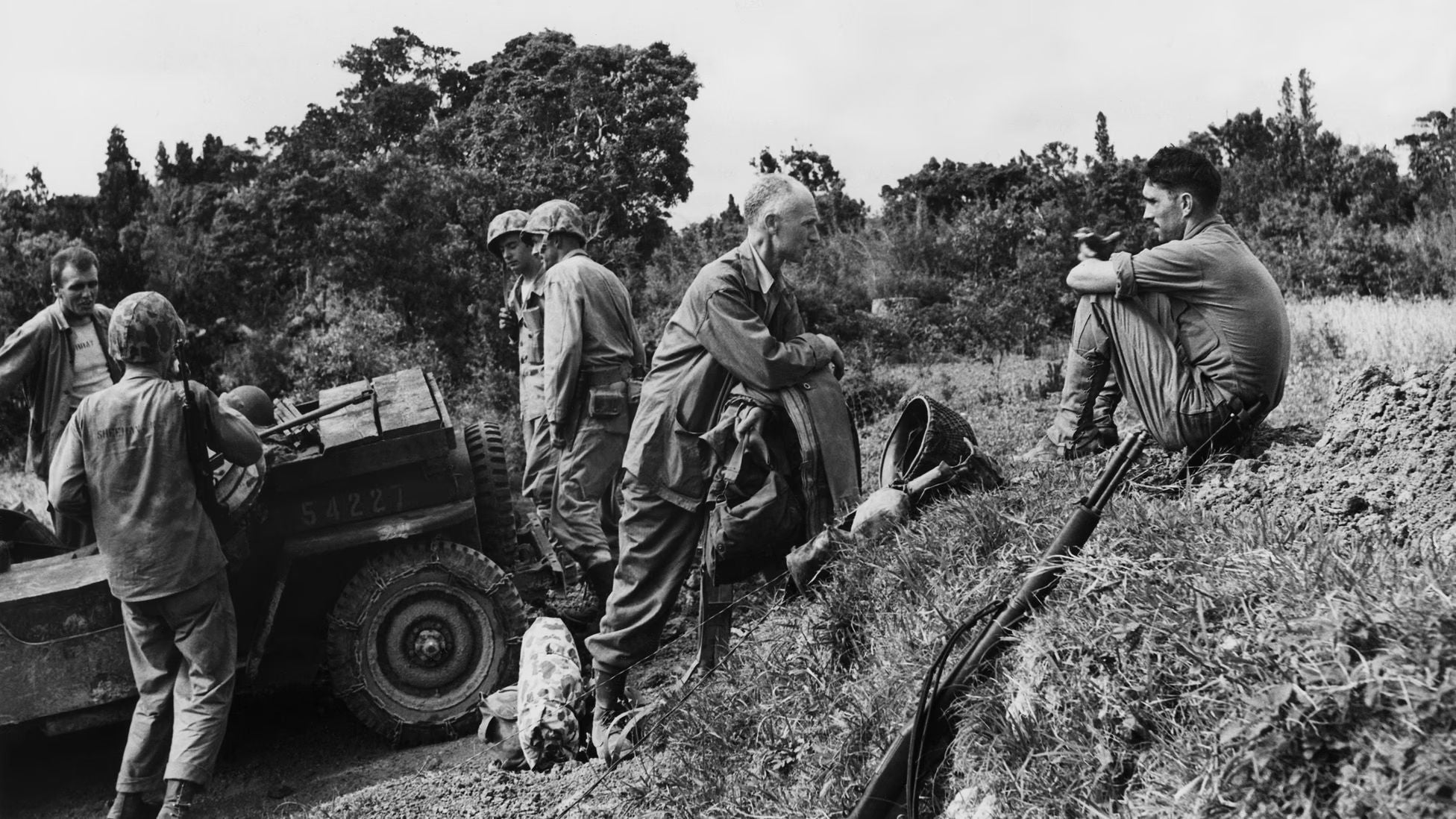 American soldiers pause beside a military vehicle during World War II as war correspondent Ernie Pyle speaks with servicemen near the front lines.