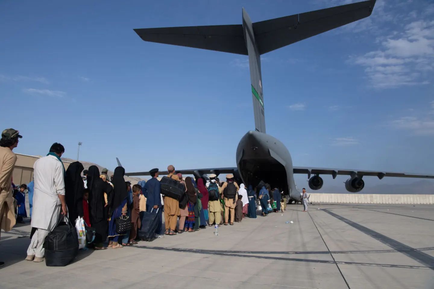 Afghan civilians carrying luggage and personal belongings line up on the tarmac to board a U.S. Air Force C-17 Globemaster III transport aircraft during the evacuation from Kabul, Afghanistan, in August 2021.