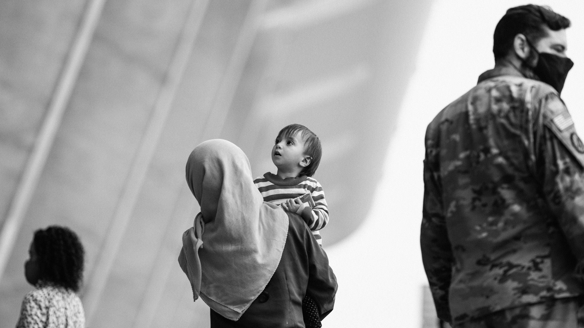 Afghan refugee mother holding a young child while standing near a U.S. service member, symbolizing the resettlement of Afghan evacuees in America.