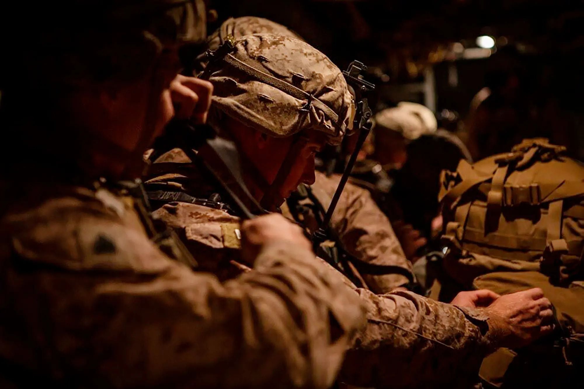 U.S. Marines sit closely together inside a dimly lit military vehicle during a nighttime operation, checking equipment and preparing for deployment.