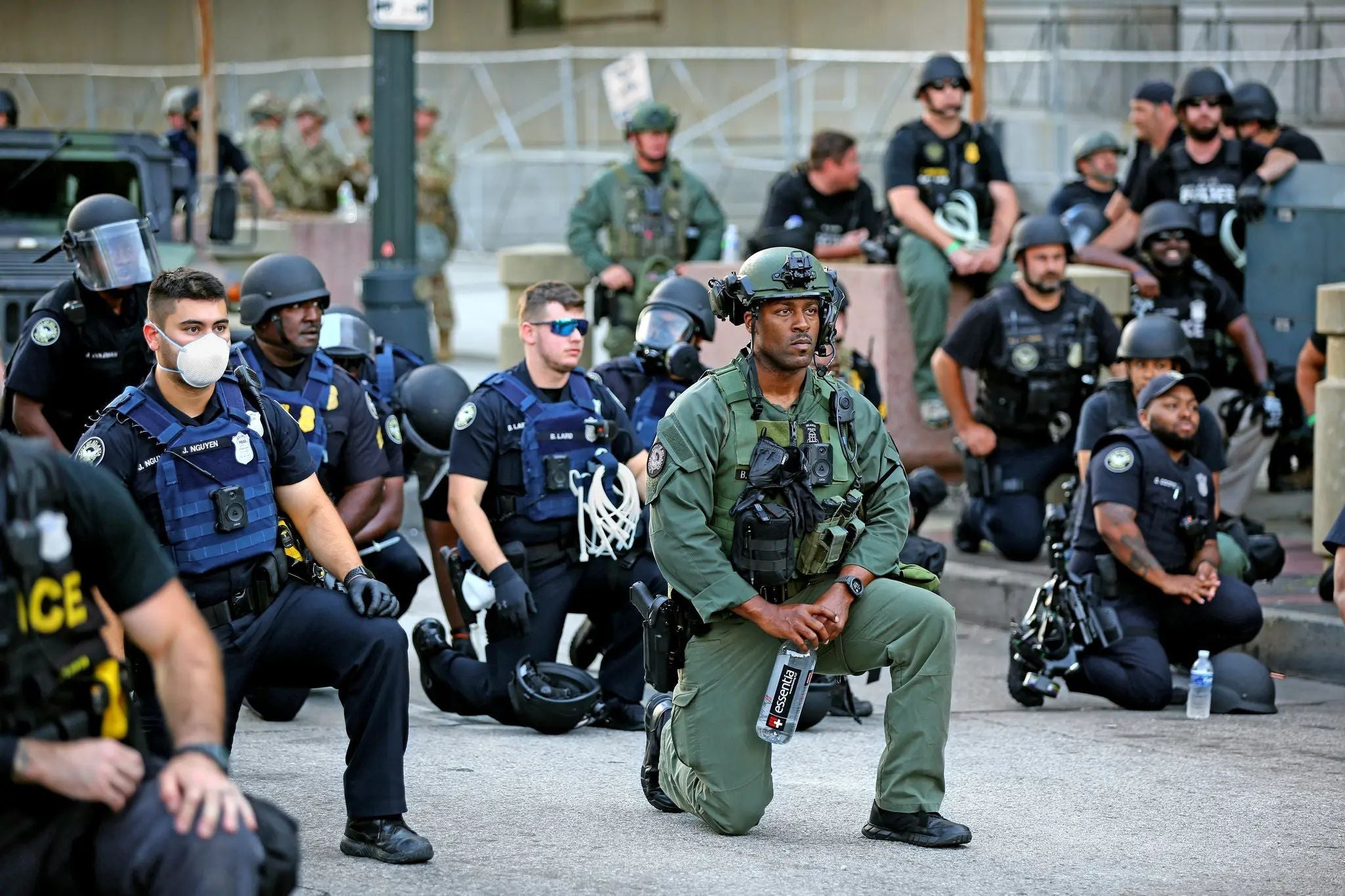 Police officers and tactical law enforcement personnel kneel together during a peaceful demonstration following the killing of George Floyd, symbolizing solidarity with protesters and calls for police reform and community trust.