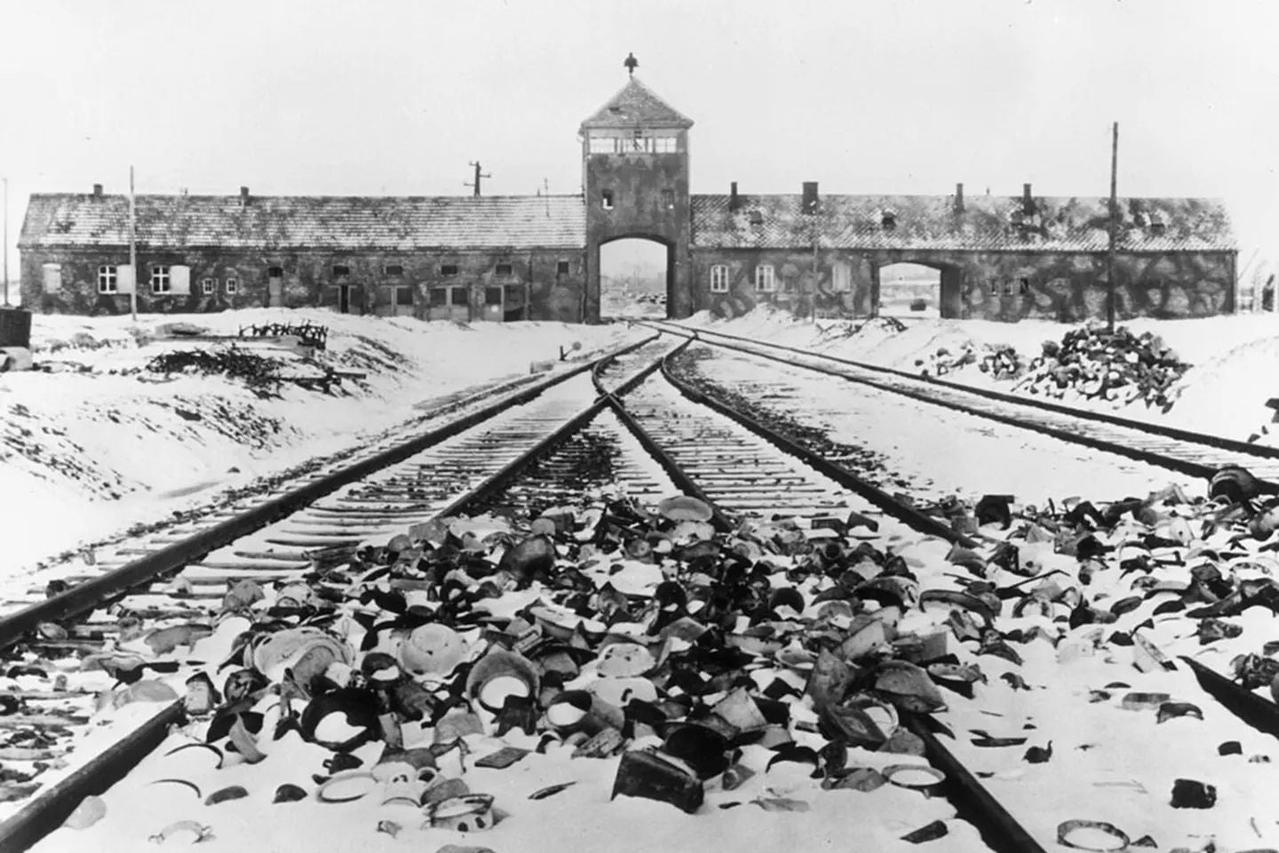 Historic black-and-white photograph of the main entrance to the Auschwitz concentration camp in Nazi-occupied Poland during winter.