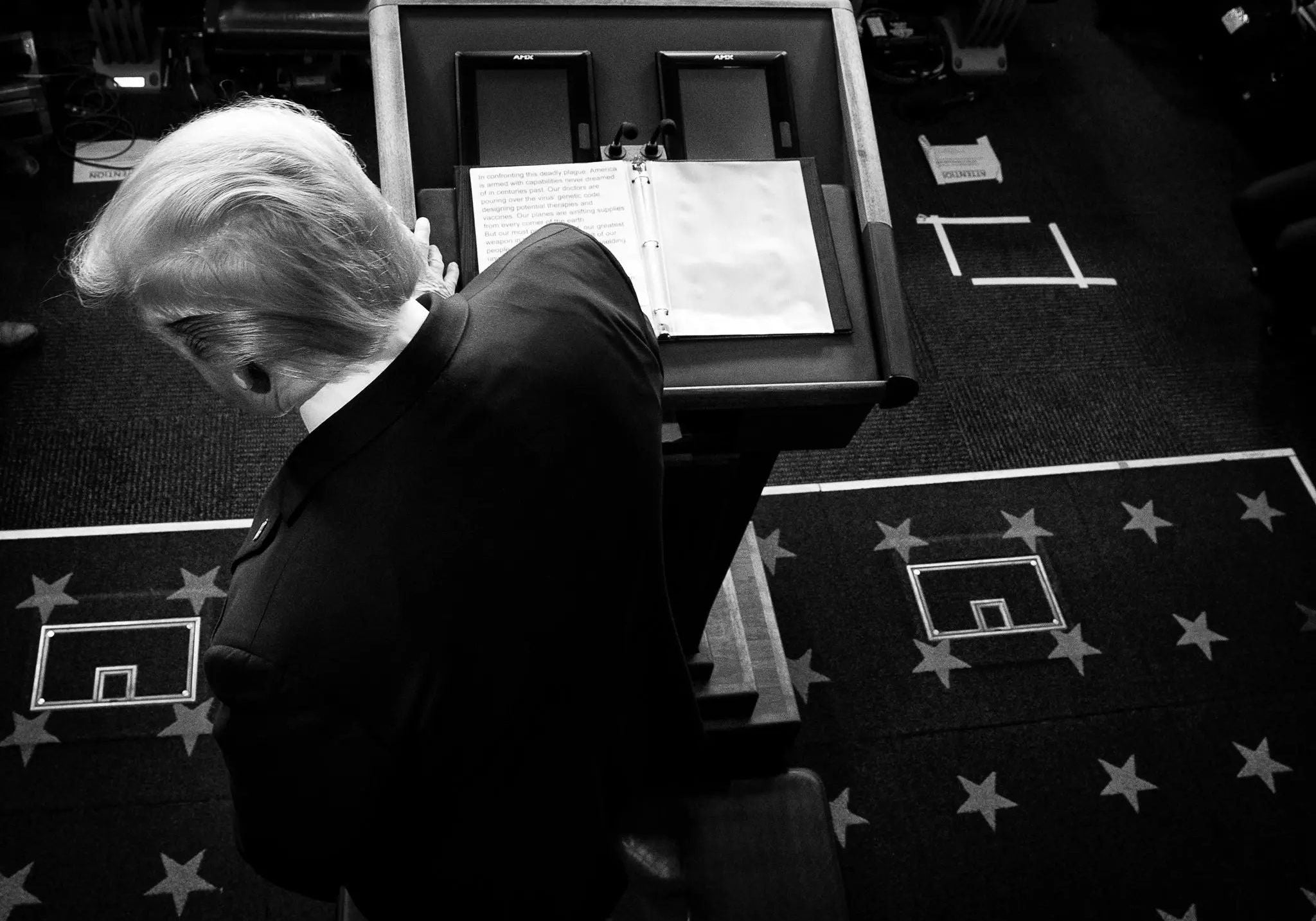 President Donald Trump stands at a White House podium during a COVID-19 press briefing, viewed from above in black and white, symbolizing presidential leadership, crisis communication, and the national response to the coronavirus pandemic.