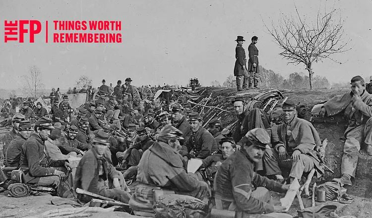Historic Civil War soldiers gather in a field encampment, resting and preparing near defensive earthworks, in a black-and-white photograph associated with Memorial Day remembrance and military sacrifice.