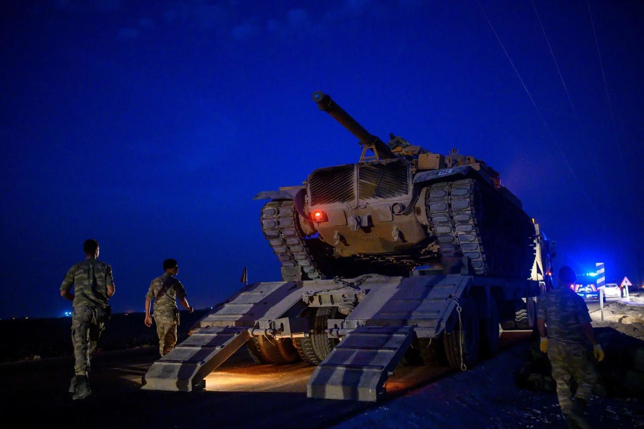 A tracked military tank is loaded onto a heavy transport trailer during a nighttime operation as soldiers supervise the movement.