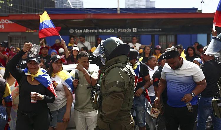 Venezuelan civilians gather near security forces during a public demonstration, with national flags visible as armored officers stand among a crowd in Caracas following political unrest and government tensions.