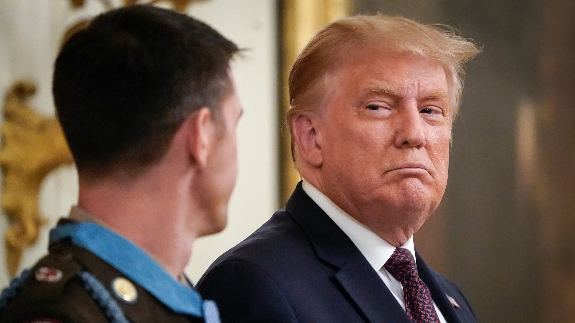 President Donald Trump looks toward a Medal of Honor recipient during a White House ceremony.