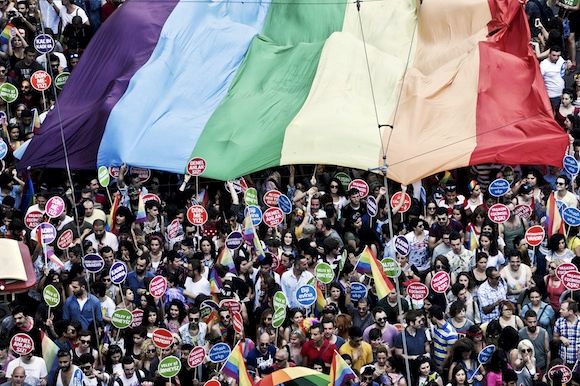A crowd at Istanbul's pride march holds up a large rainbow flag and protest signs.
