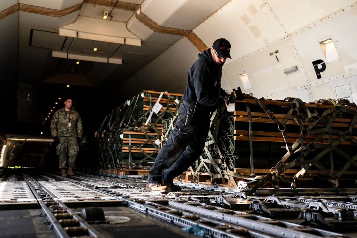 Military personnel load palletized military aid onto a cargo aircraft, illustrating the large-scale logistics and international effort required to transport weapons, ammunition, and supplies to Ukraine during the ongoing war with Russia.