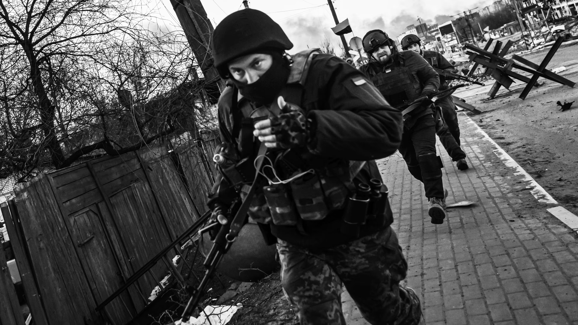 Ukrainian soldiers in full combat gear move tactically through a damaged urban street during active operations.