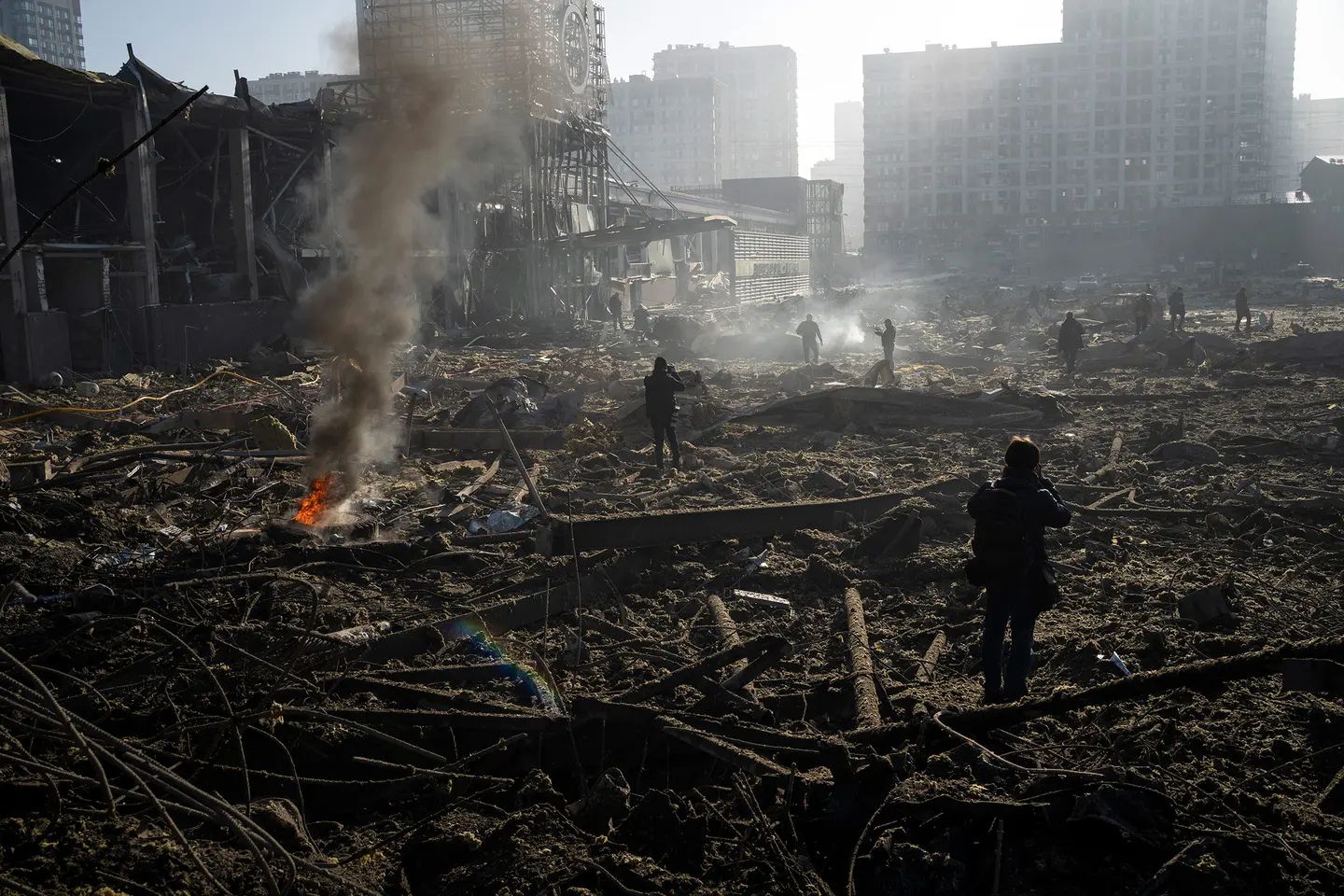 People walk through the devastated aftermath of a missile strike in a Ukrainian city, surveying smoking rubble and destroyed buildings.
