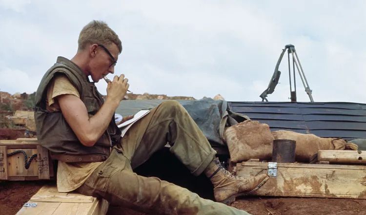 Vietnam War-era Marine sitting on an armored vehicle while writing in a notebook during combat operations in a rugged field environment