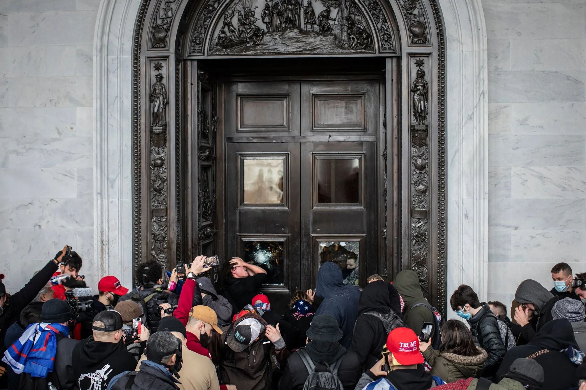 Crowd of protesters gathered outside a large government building doorway during the January 6, 2021 attack on the U.S. Capitol.