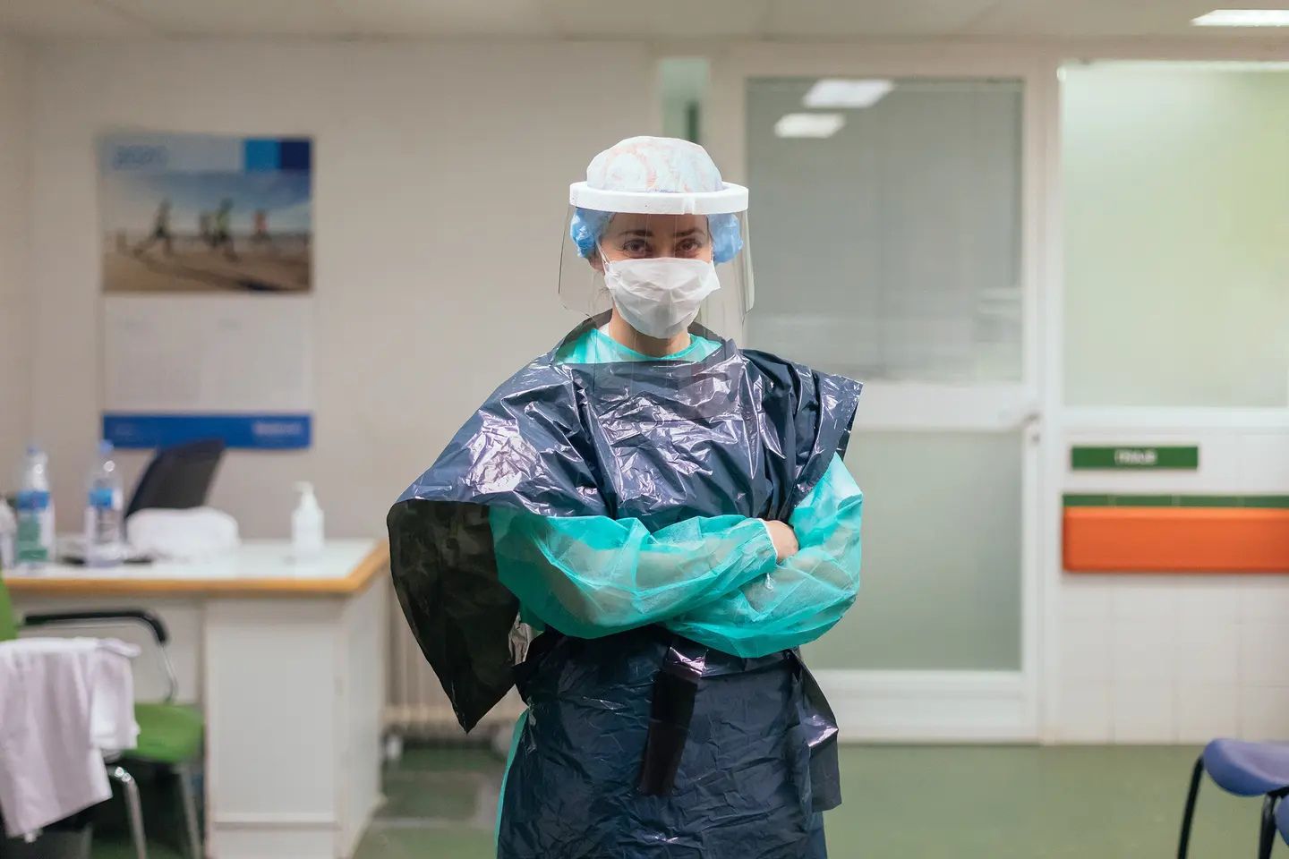 A healthcare worker wearing a face shield, surgical mask, gloves, and improvised protective gown stands inside a hospital during the COVID-19 pandemic.