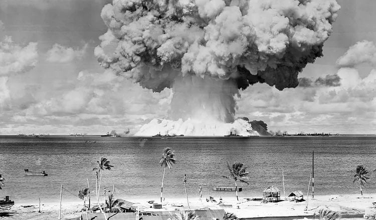 Historic black-and-white photograph of a massive nuclear mushroom cloud rising above the Pacific Ocean
