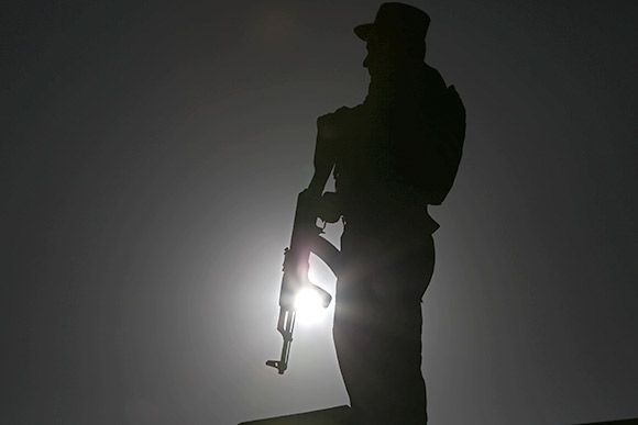 Silhouette of a soldier holding a rifle, backlit against a bright sky.