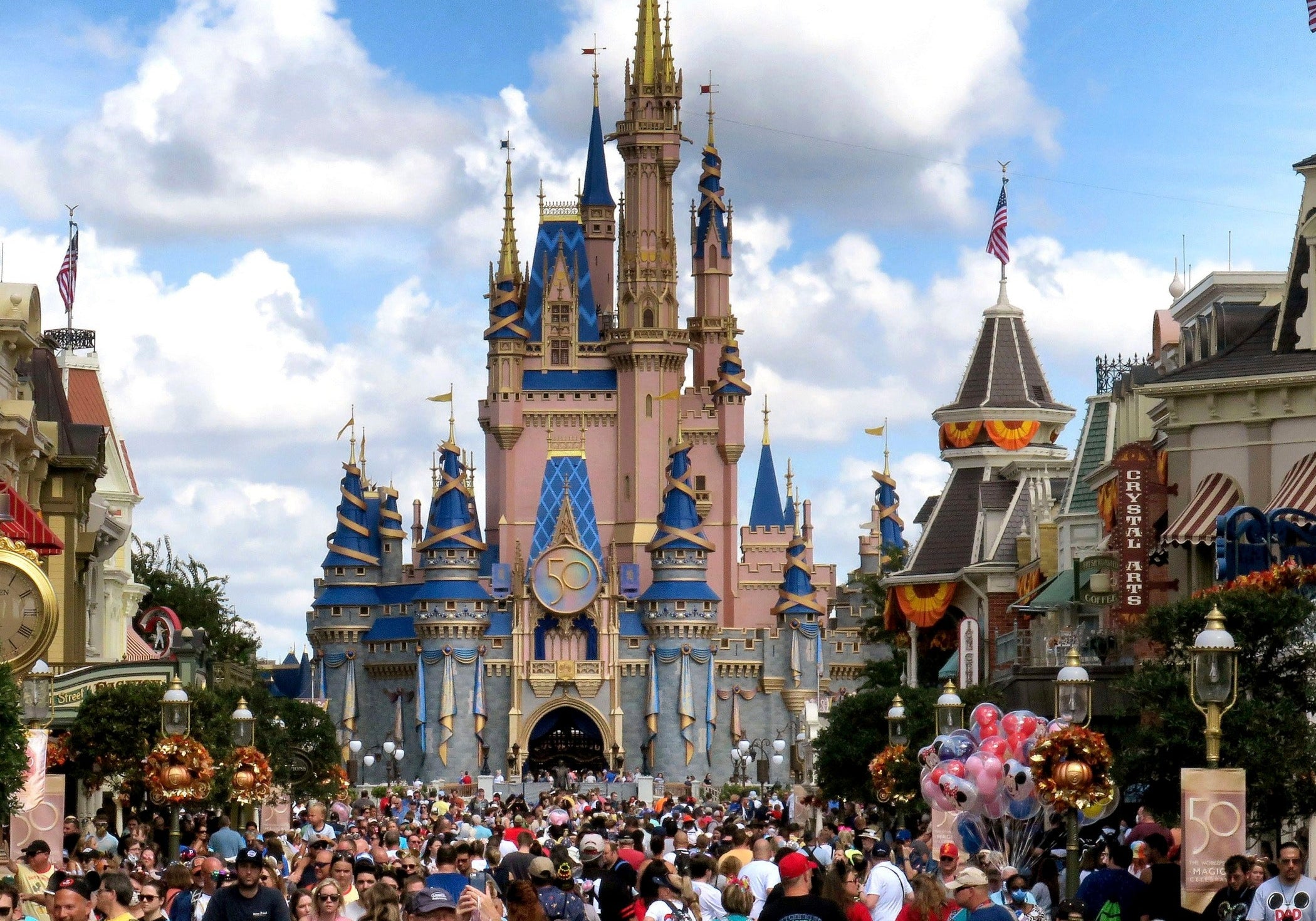 Cinderella Castle at Walt Disney World's Magic Kingdom, seen from a crowded Main Street U.S.A. beneath a partly cloudy sky.