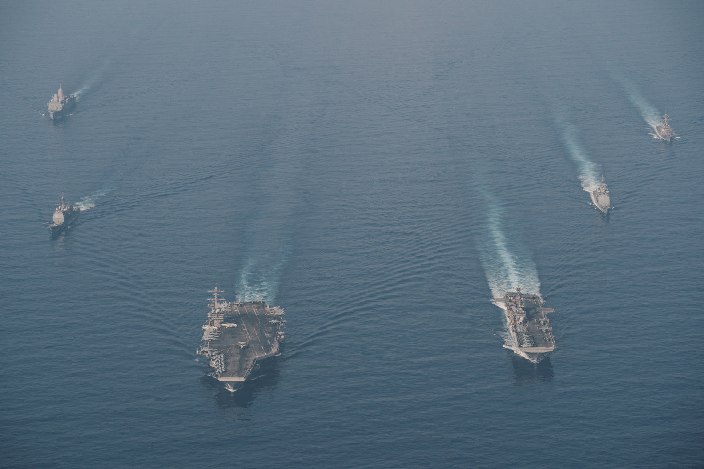 Aerial photo of a U.S. Navy carrier strike group sailing in formation at sea.