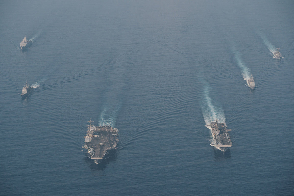 Aerial photo of a U.S. Navy carrier strike group sailing in formation at sea.